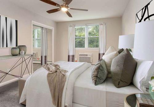 Fully furnished tan bedroom with a ceiling fan, lamps, and window at Westgate Arms apartments