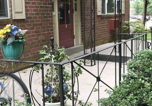 Entrance to a residential building with a porch and flowers at Westgate Arms apartments for rent
